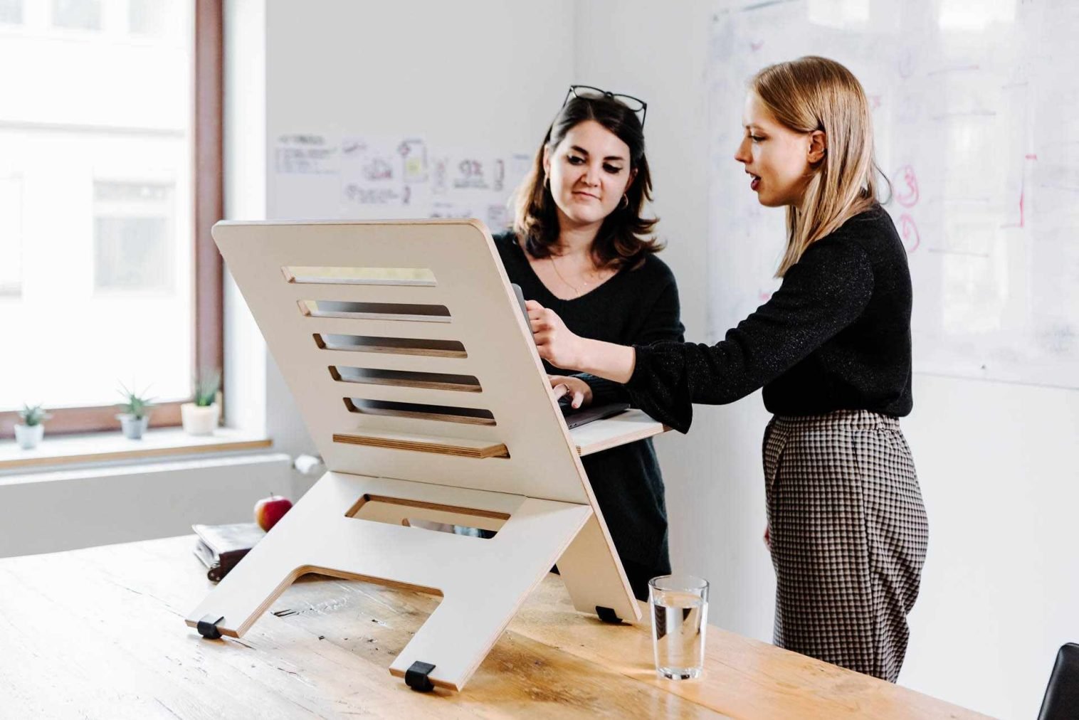 A female coach and her client at a standing desk in a creative office space, sharing ideas.